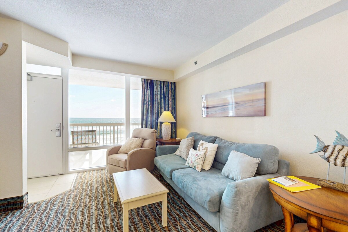 A hotel room with a balcony, a sofa, a table, and a lamp.