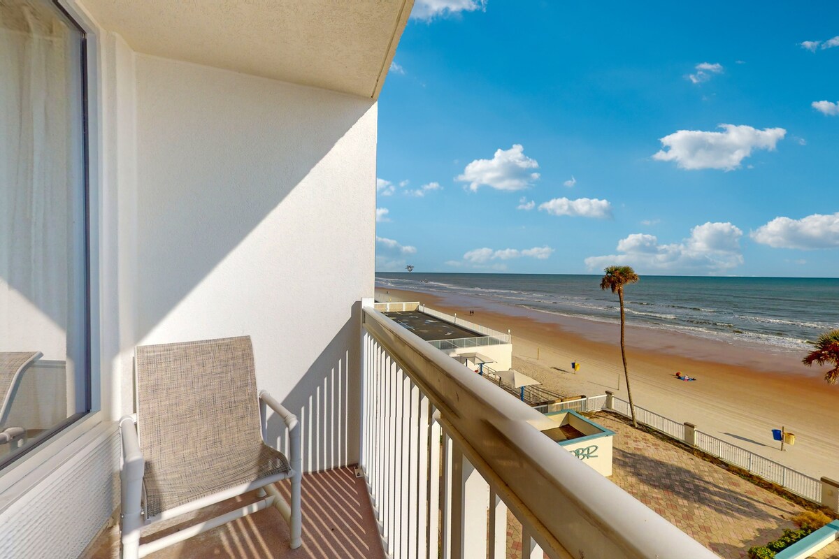 A balcony with a view of a beach, a palm tree, and a clear sky.