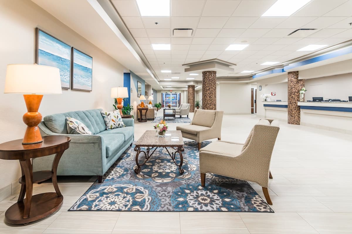 A spacious lobby with a blue patterned rug, a blue sofa, a coffee table, and a beige armchair.
