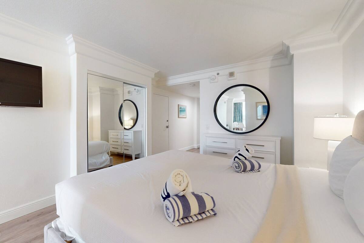 A hotel room with a large bed, two bedside tables, a mirror, and a wardrobe.