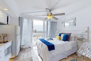 A hotel room with a bed, a desk, a chair, a ceiling fan, and a view of the city. - Daytona Beach VI (Daytona Beach)