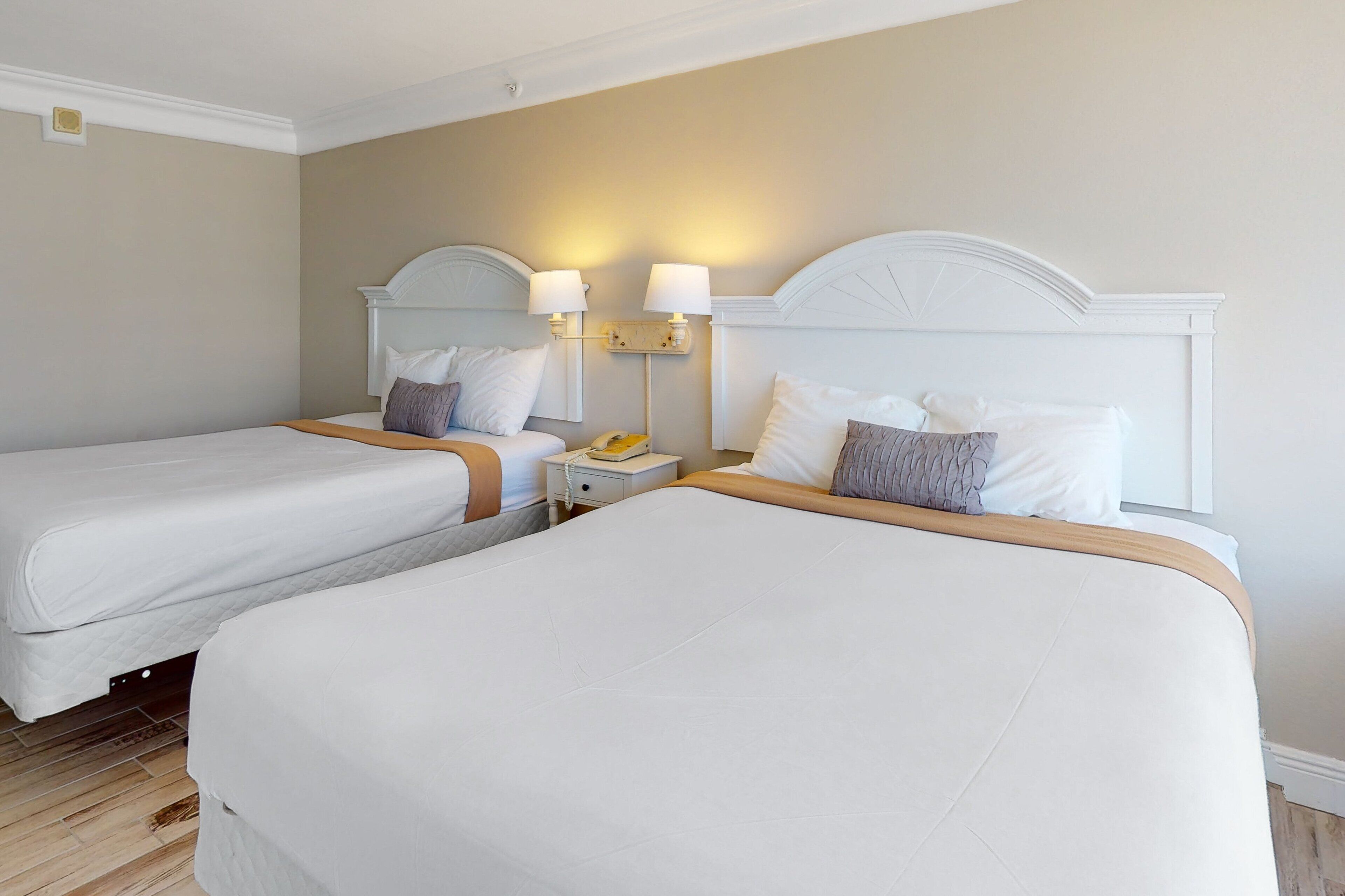Une chambre d’hôtel avec deux lits, une table de chevet avec une lampe et un téléphone fixé au mur.
