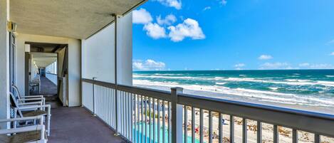 A balcony with a view of the ocean and a pool area.