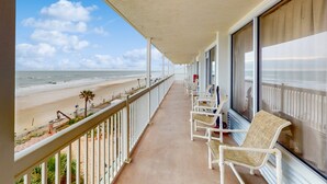 Ein Balkon mit Blick auf den Strand, weiße Korbstühle und ein überdachter Gang.