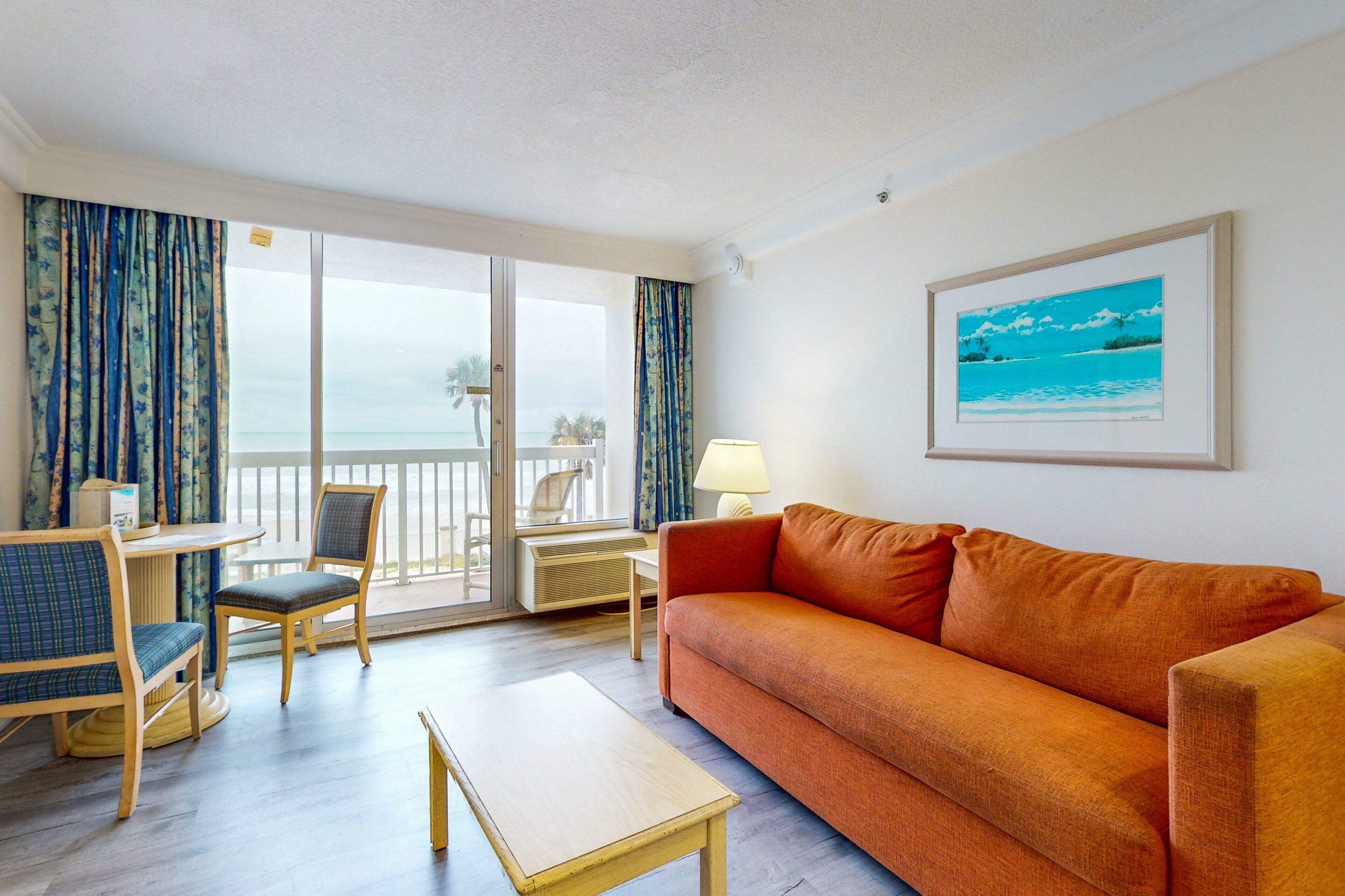 Quarto de hotel com varanda, sofá, mesa e cadeira.