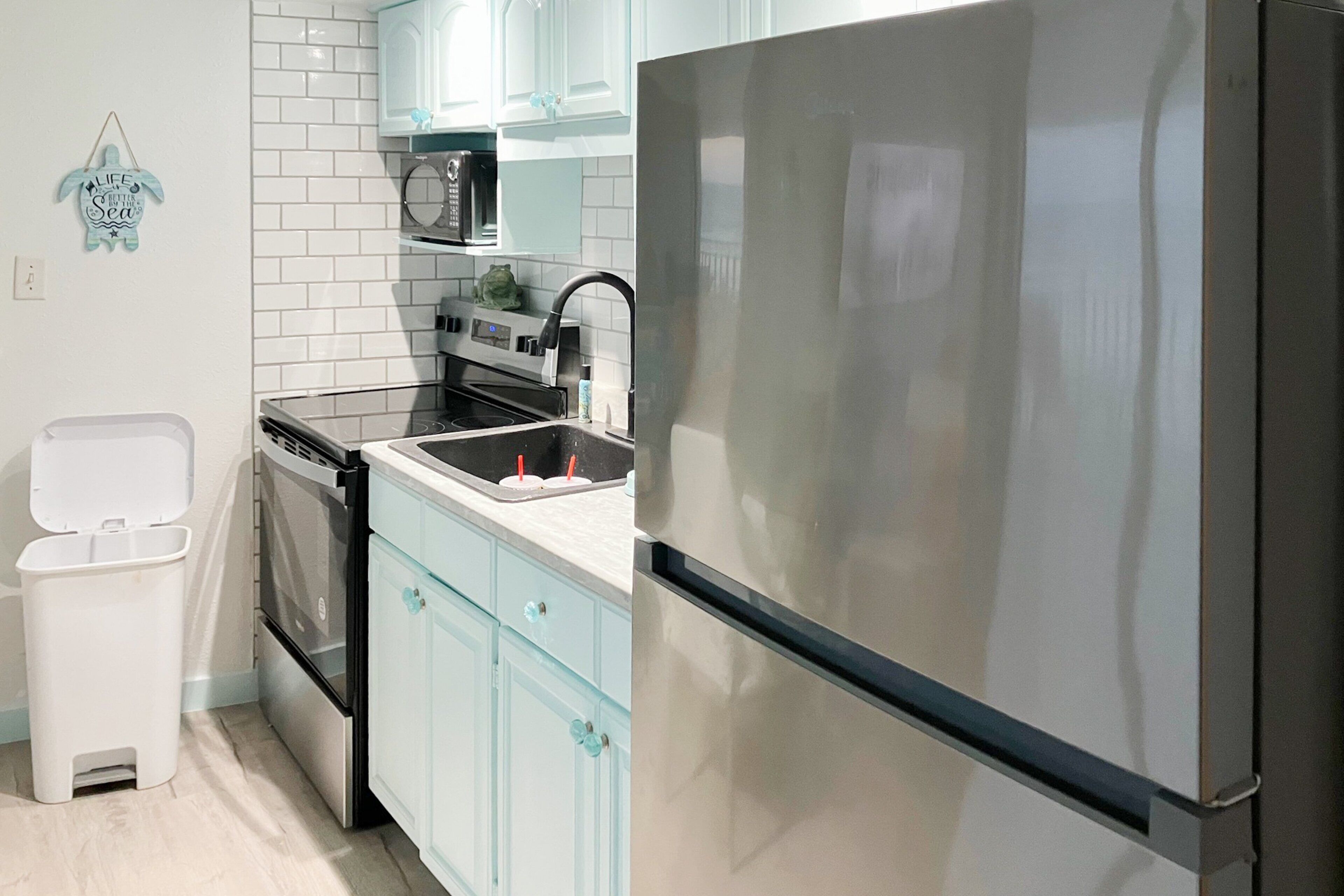 A modern kitchen with stainless steel appliances, light blue cabinets, and white subway tiles.