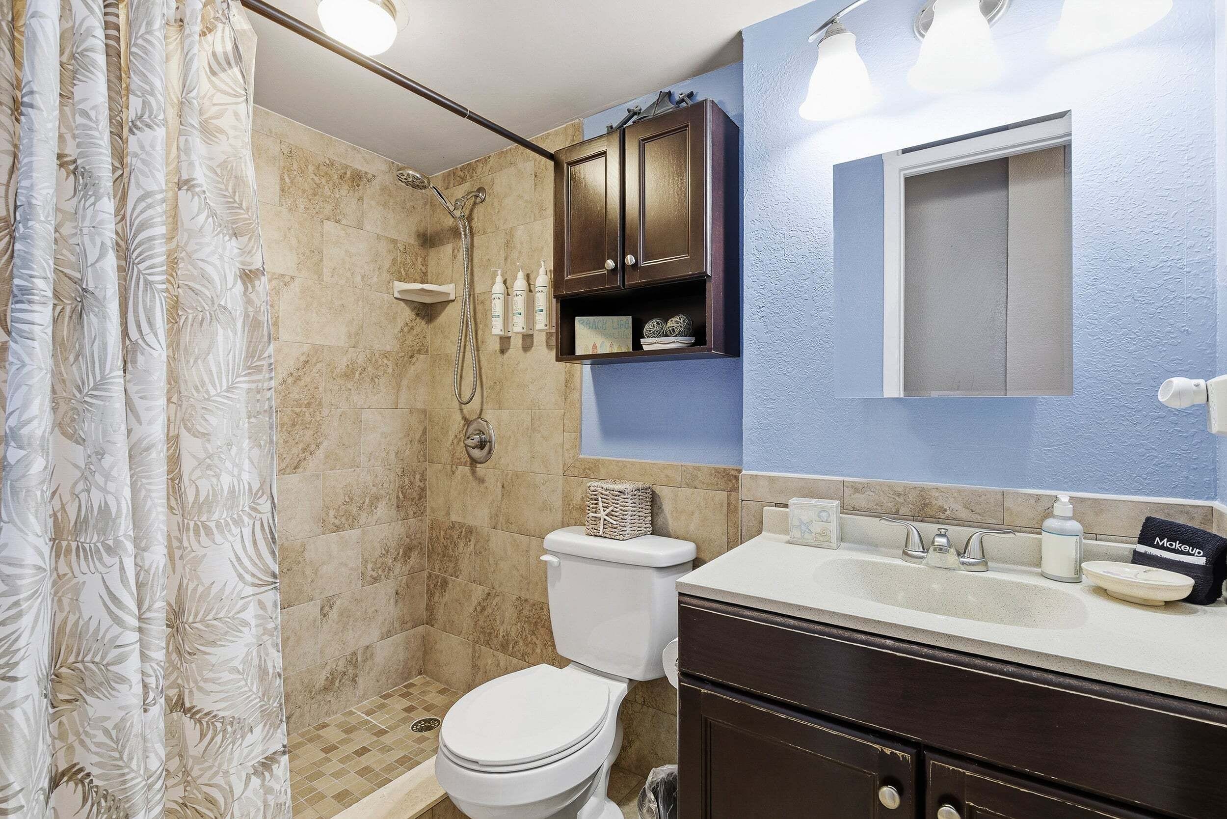 A bathroom with a shower, toilet, vanity, and a mirror.