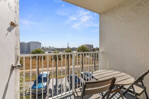 A balcony with a table and chairs, overlooking a parking area with several cars and buildings in the background. - Daytona Ocean Jewels (Daytona Beach)