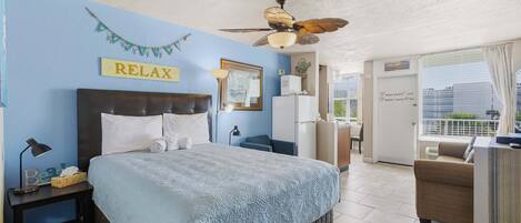 A bedroom with a bed, a nightstand, a desk, a ceiling fan, a window, and a balcony.