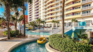 Un espace piscine d’hôtel comprenant une piscine circulaire, des palmiers et un immeuble à plusieurs étages doté de balcons.