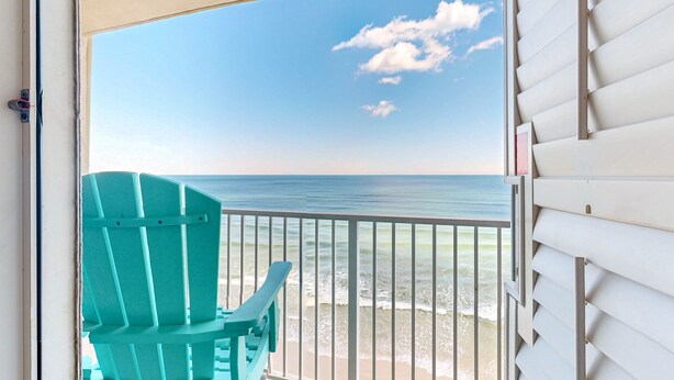 A turquoise chair on a balcony overlooking a beach with a clear sky and calm sea. - Daytona Pirates Cove (Daytona Beach Shores)