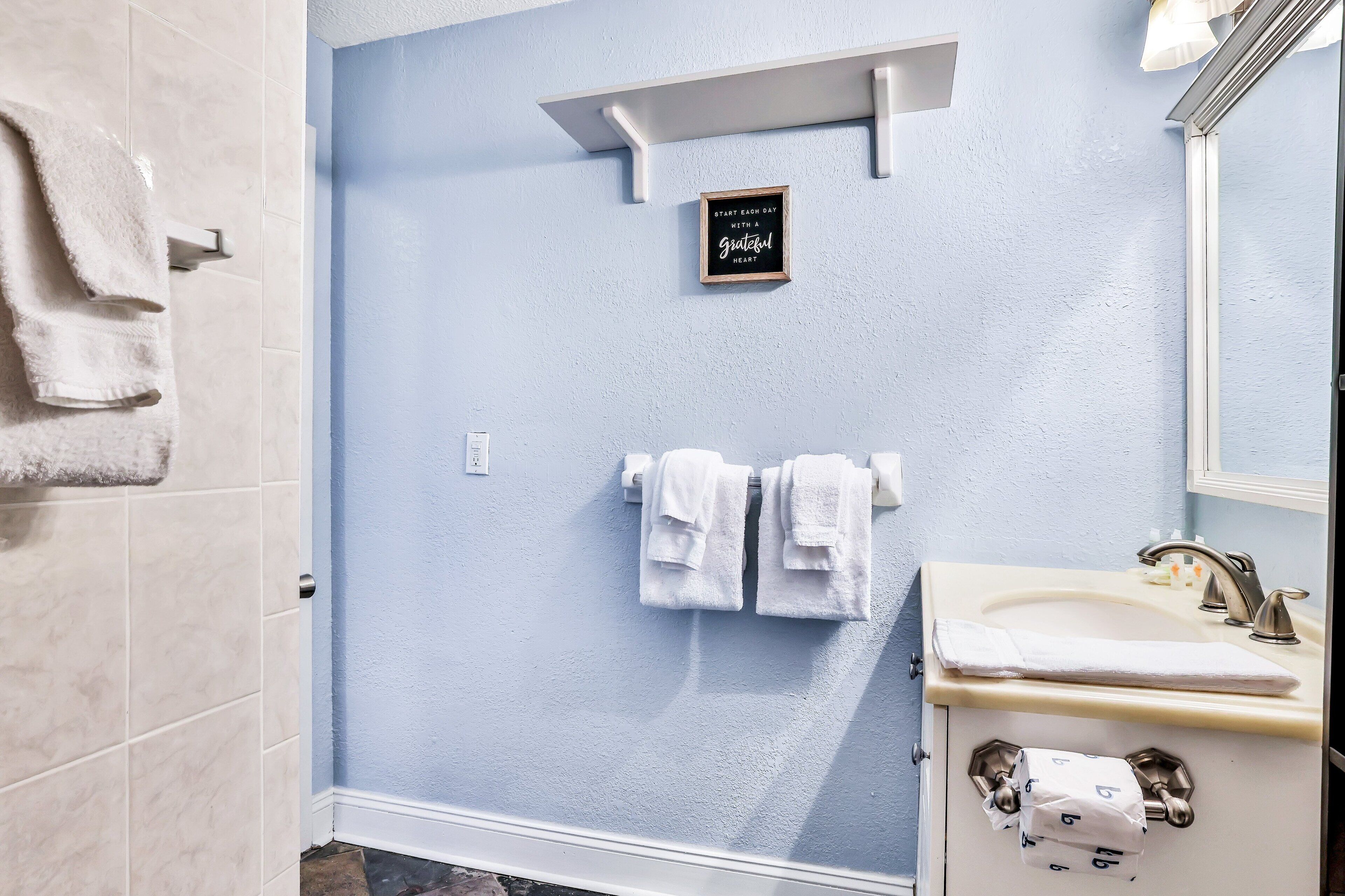 A bathroom with a light blue wall, a white sink, and two white towels hanging on the wall.