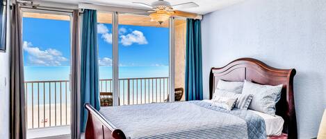 Un dormitorio con cama, ventilador de techo y vista a la playa a través de amplias ventanas.