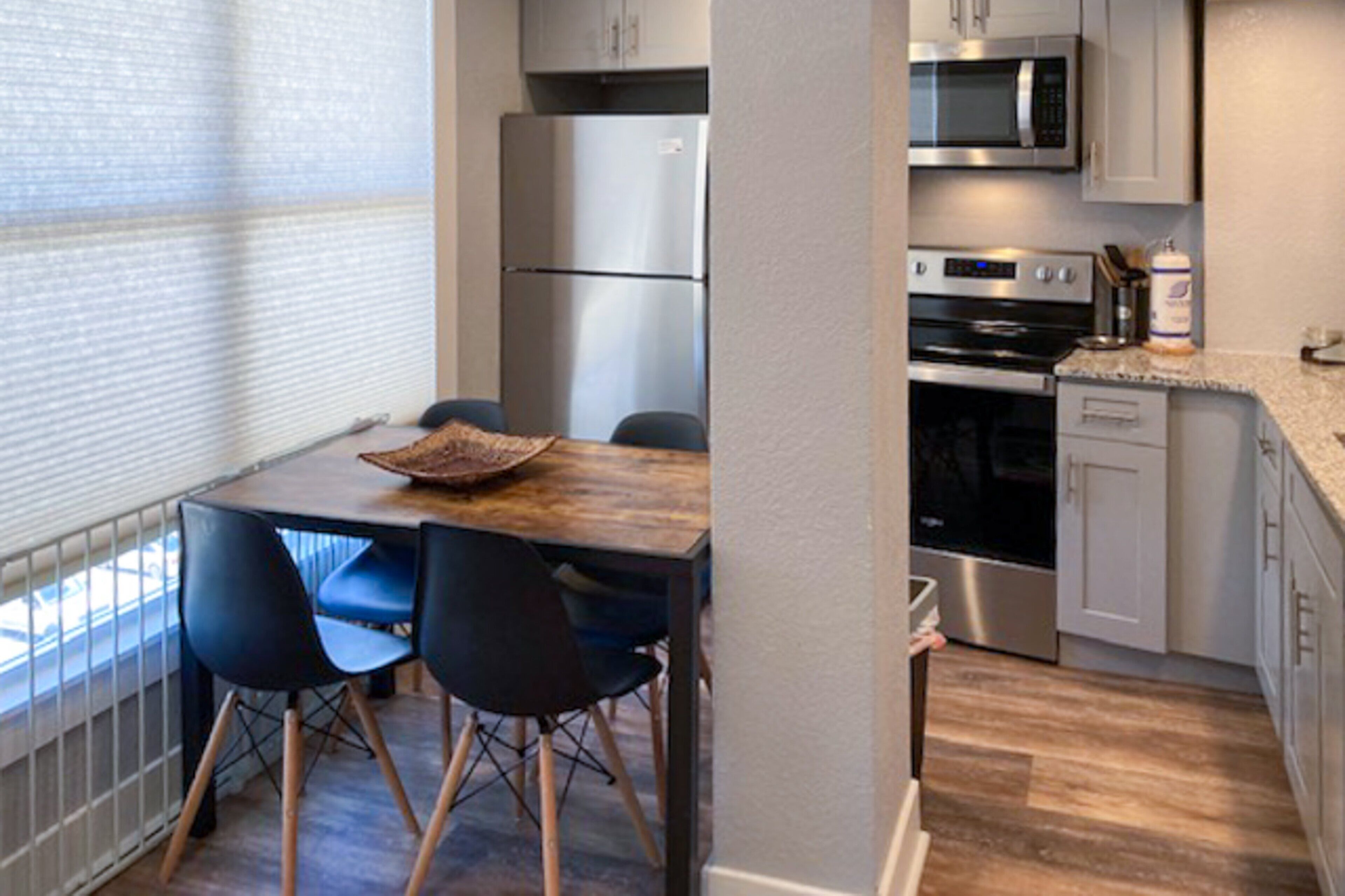 A compact kitchen with a wooden table, four chairs, a refrigerator, a microwave, an oven, and a dishwasher.