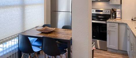 A compact kitchen with a wooden table, four chairs, a refrigerator, a microwave, an oven, and a dishwasher.