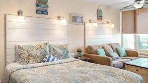 A bedroom with a large bed, a sofa, and a small table. There are wall-mounted lights and a ceiling fan. - Daytona Pirates Cove (Daytona Beach Shores)