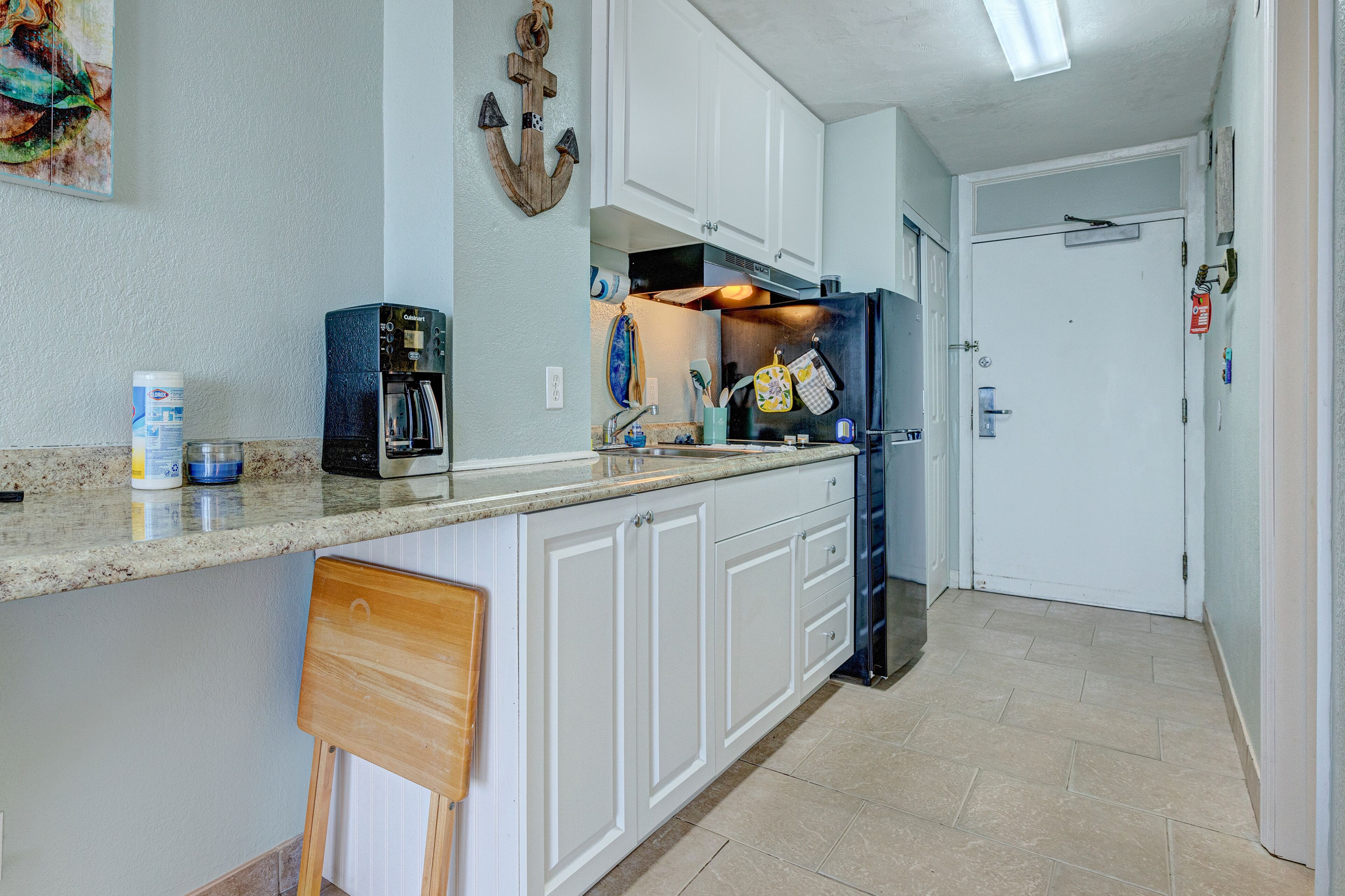 A kitchen with white cabinets, a wooden chair, and a coffee maker.
