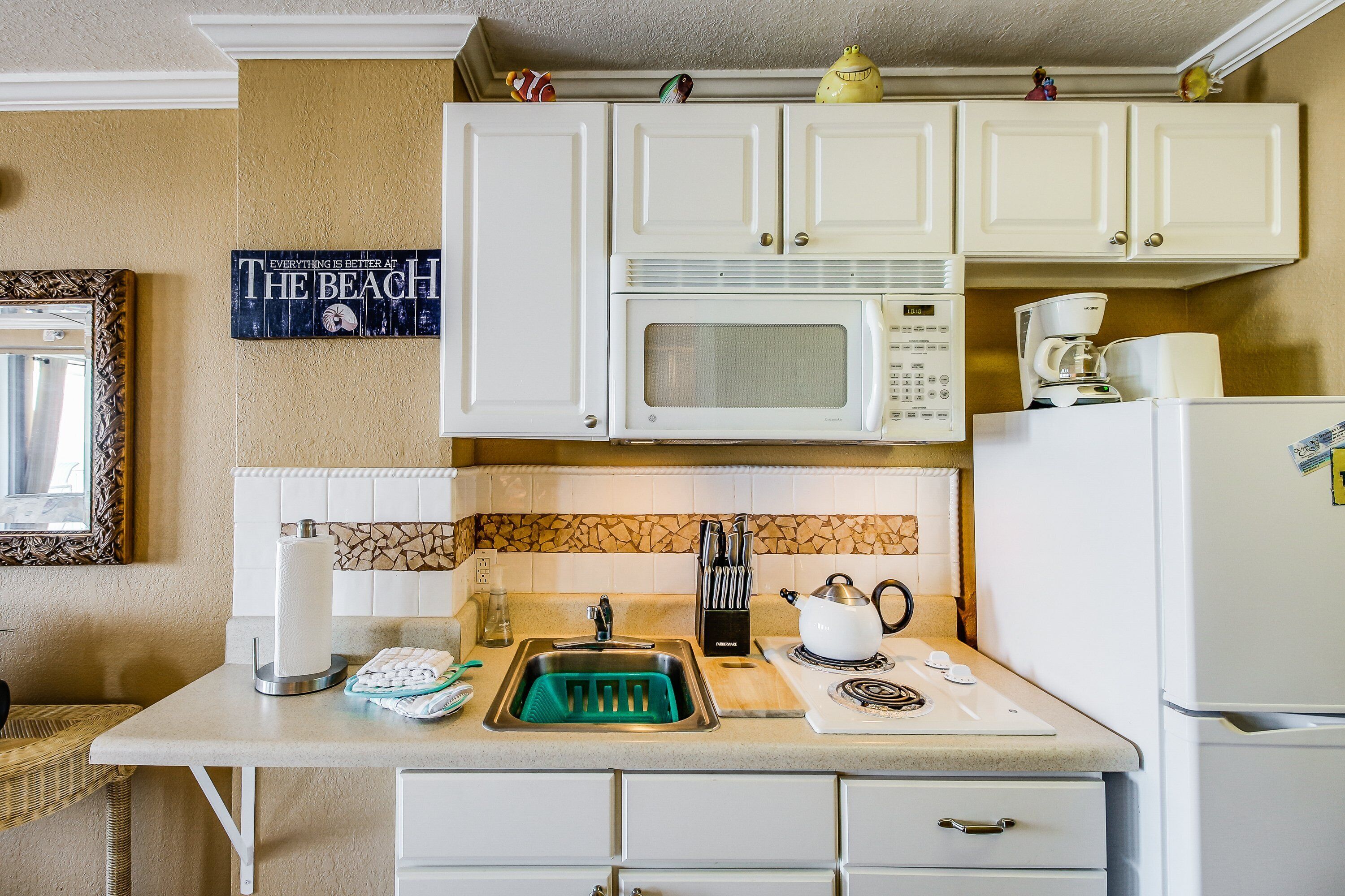 A kitchen with white cabinets, a microwave, a coffee maker, and a sink with a green soap dish.
