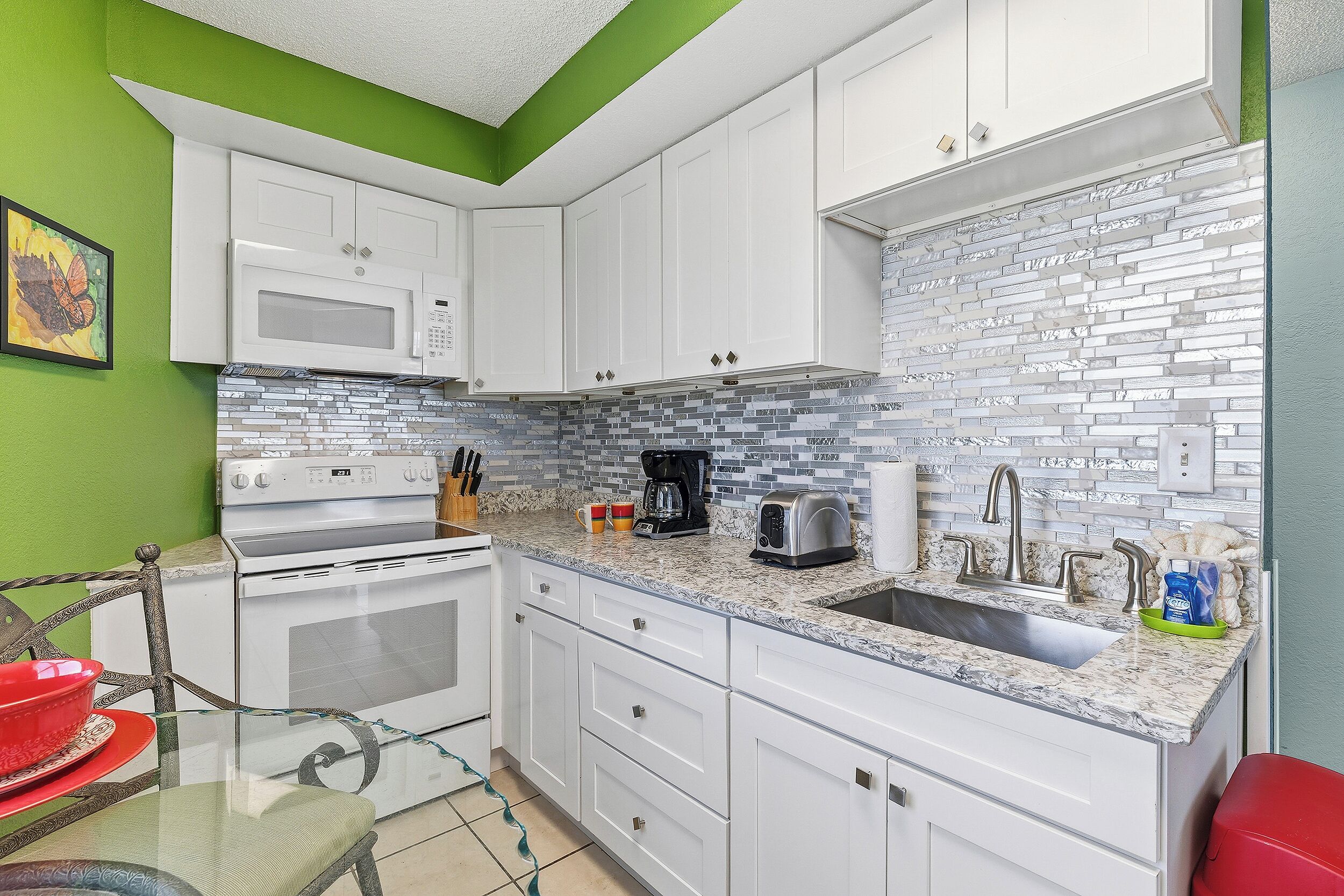 A kitchen with white cabinets, a microwave, a stove, a sink with a modern faucet, and a tiled backsplash.