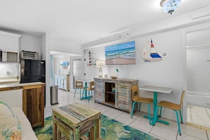 Una cocina moderna con un refrigerador negro, un mueble de madera y un comedor con sillas turquesa y una mesa blanca.