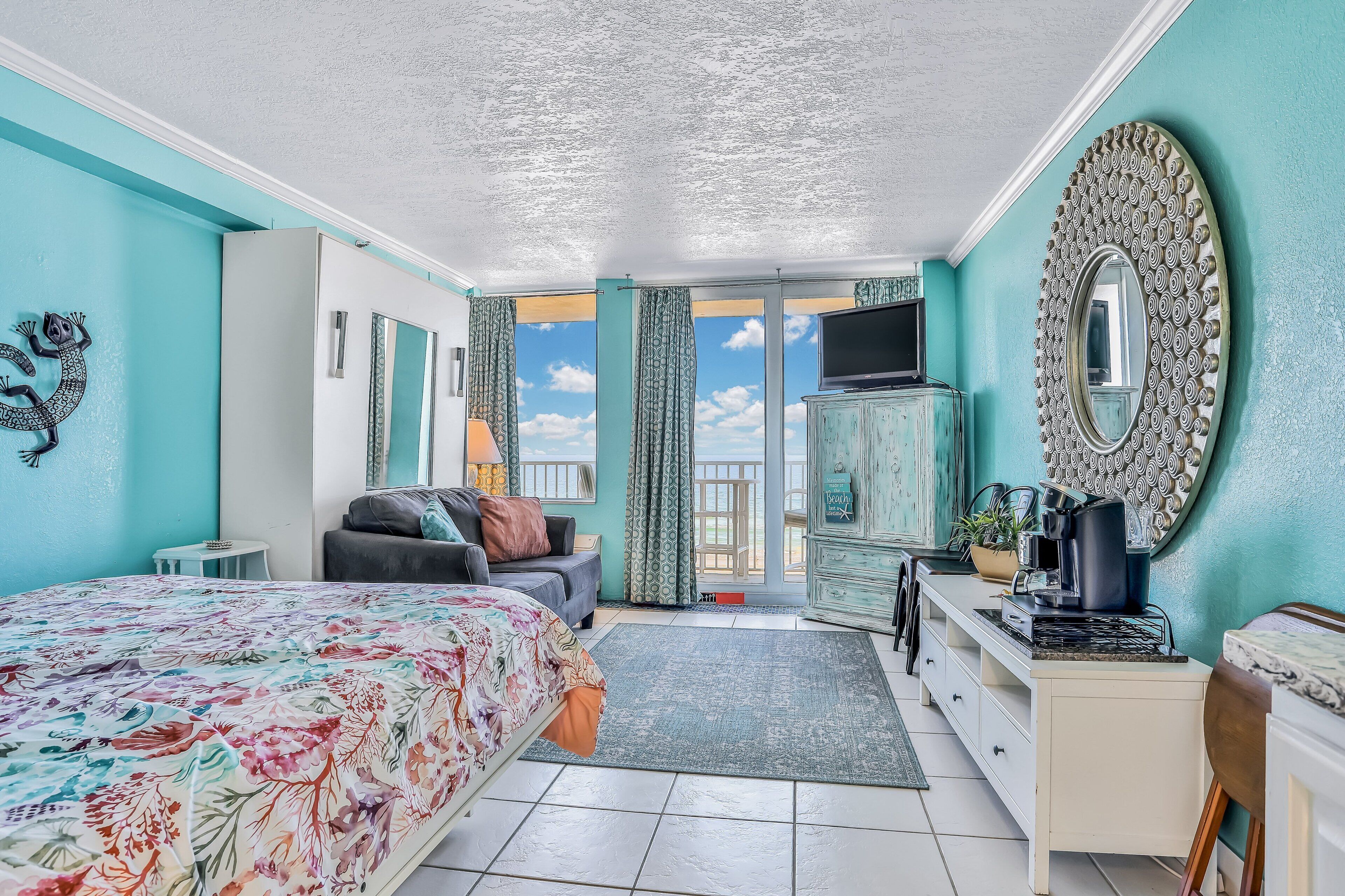 Un dormitorio con cama, cómoda, televisor y vista al cielo a través de la puerta.