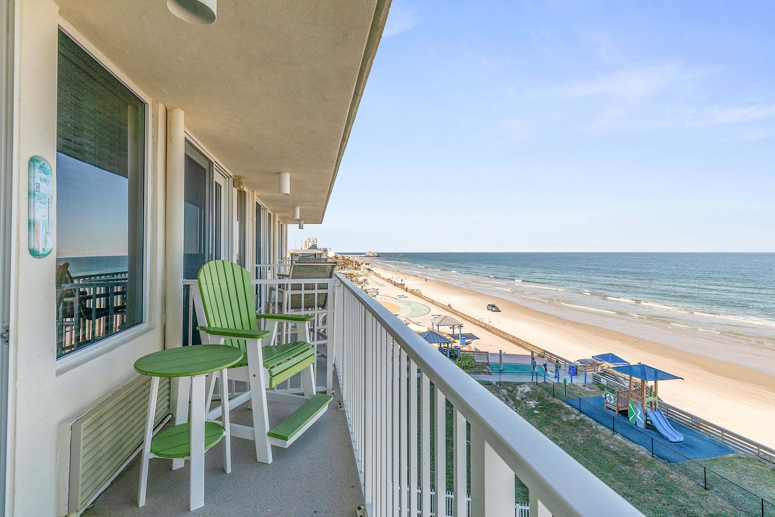 A balcony with a view of the beach, a pool, and a playground.
