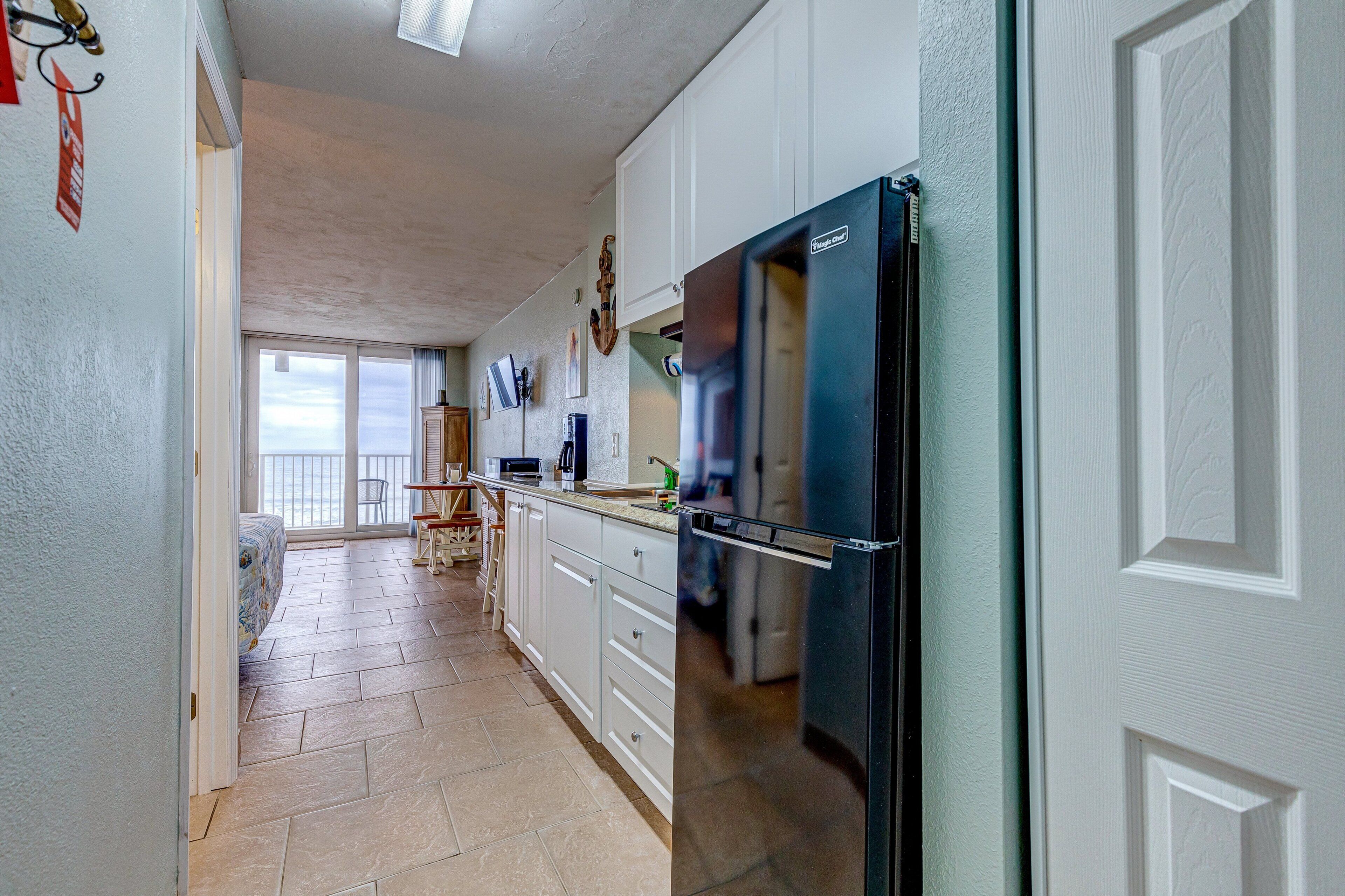 A kitchen with white cabinets, a black refrigerator, and a herringbone floor pattern.