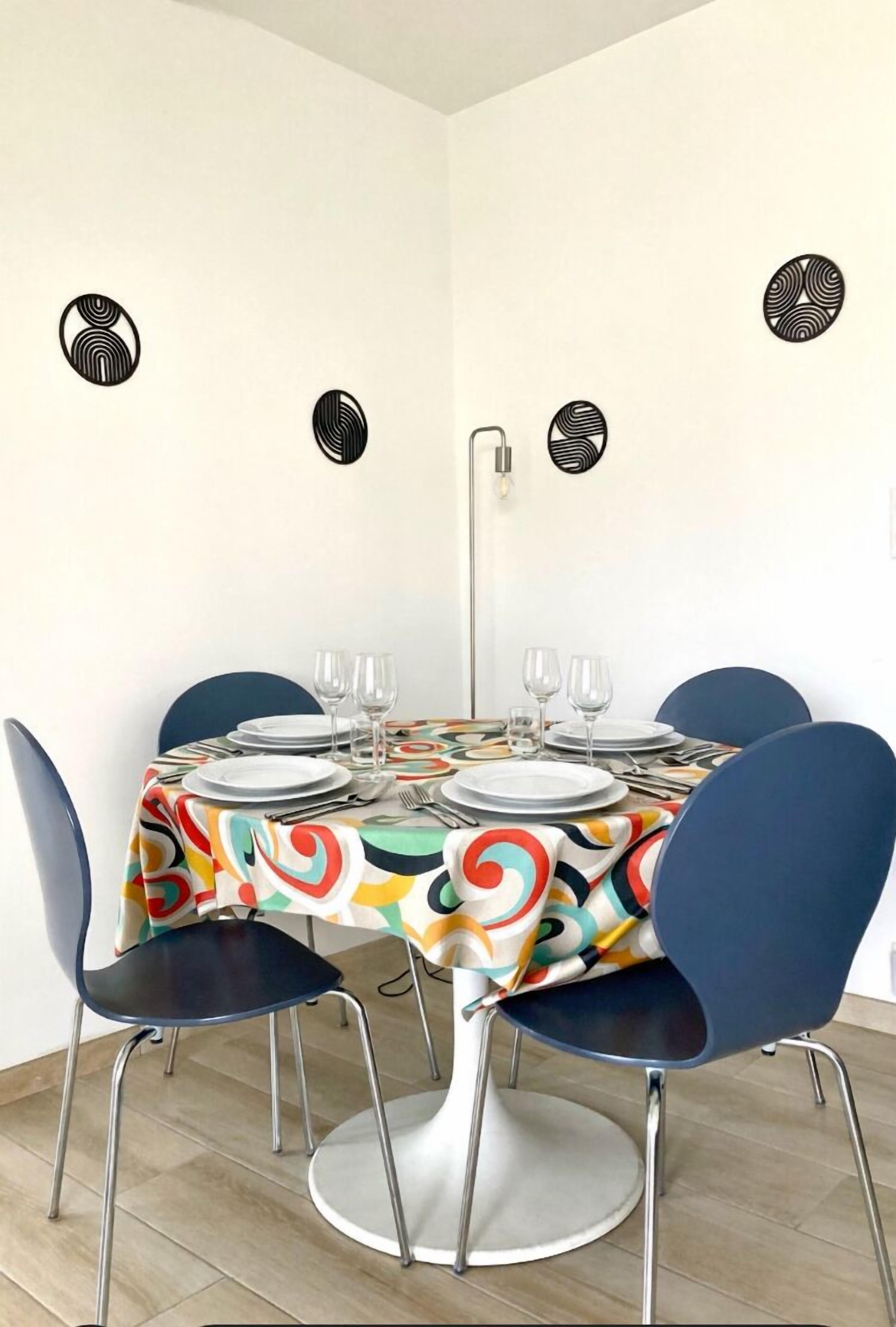Uma mesa de jantar posta com pratos, copos e talheres, rodeada por cadeiras azuis.