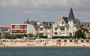 A beach with people swimming and sunbathing, and a row of buildings with varied architectural styles. - APARTMENT 100 M FROM THE BEACH (Saint-Georges-de-Didonne)