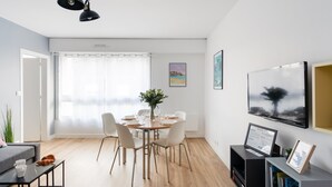 Uma sala de estar moderna com área de jantar, piso de madeira, um sofá cinza, uma mesa de centro e uma TV em um móvel.