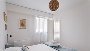 Quarto moderno com cama grande, mesa de cabeceira com abajur, quadro na parede e janela com cortinas.