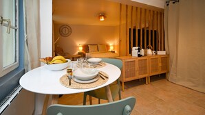 A cozy room with a bed, bedside table, and a dining area with a table set for two. - Studio Cocon Landon - Studio Apartment, Sleeps 2 (Château-Landon)