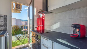 Une cuisine moderne avec une machine à café Bosch rouge, un plan de travail noir et une vue sur un jardin verdoyant par une porte ouverte.