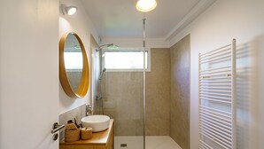 Ein modernes Badezimmer mit rundem Spiegel, Waschbecken, Dusche und Handtuchhalter.