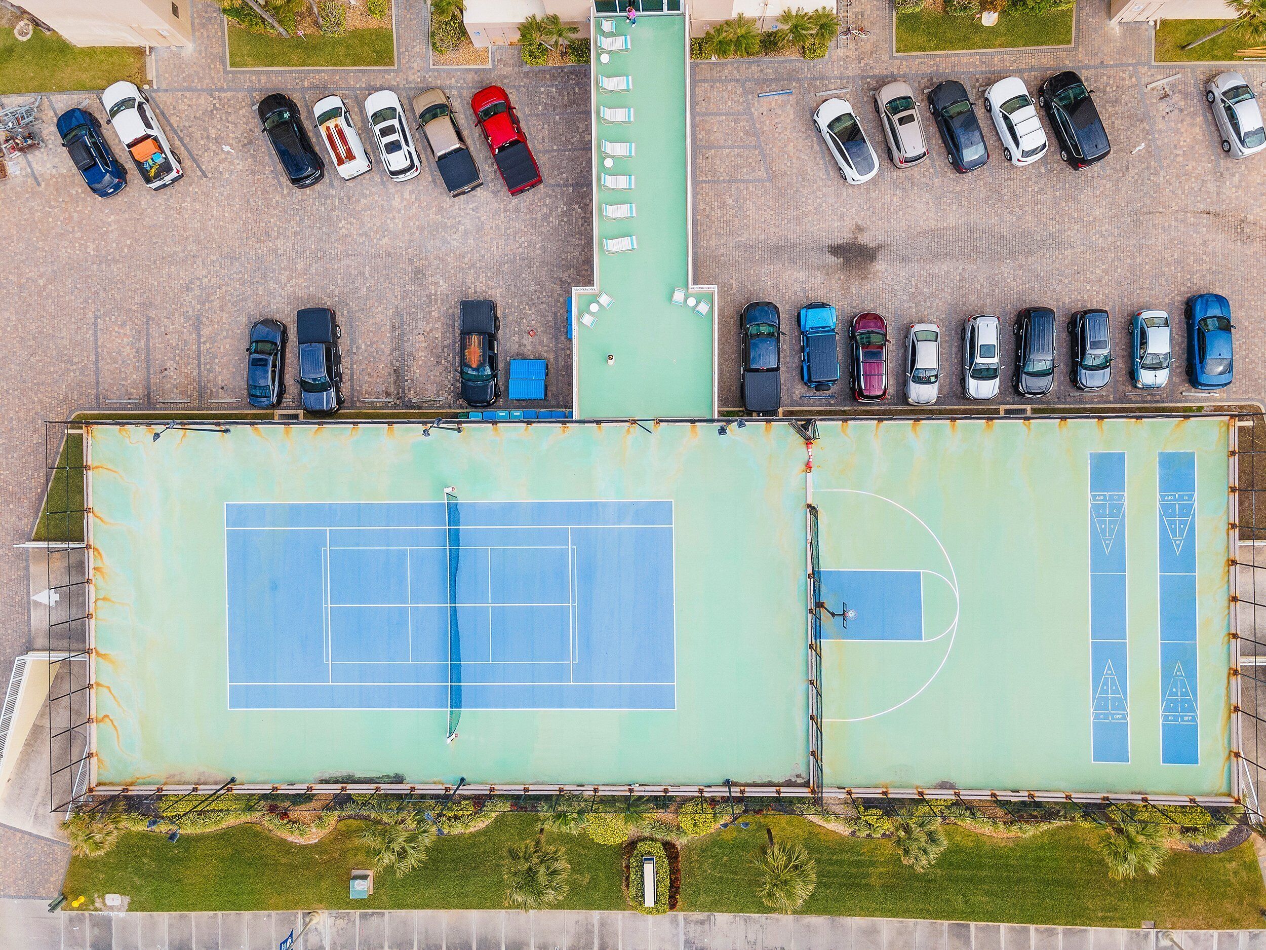 An aerial view of a parking lot with multiple rows of cars and a tennis court.