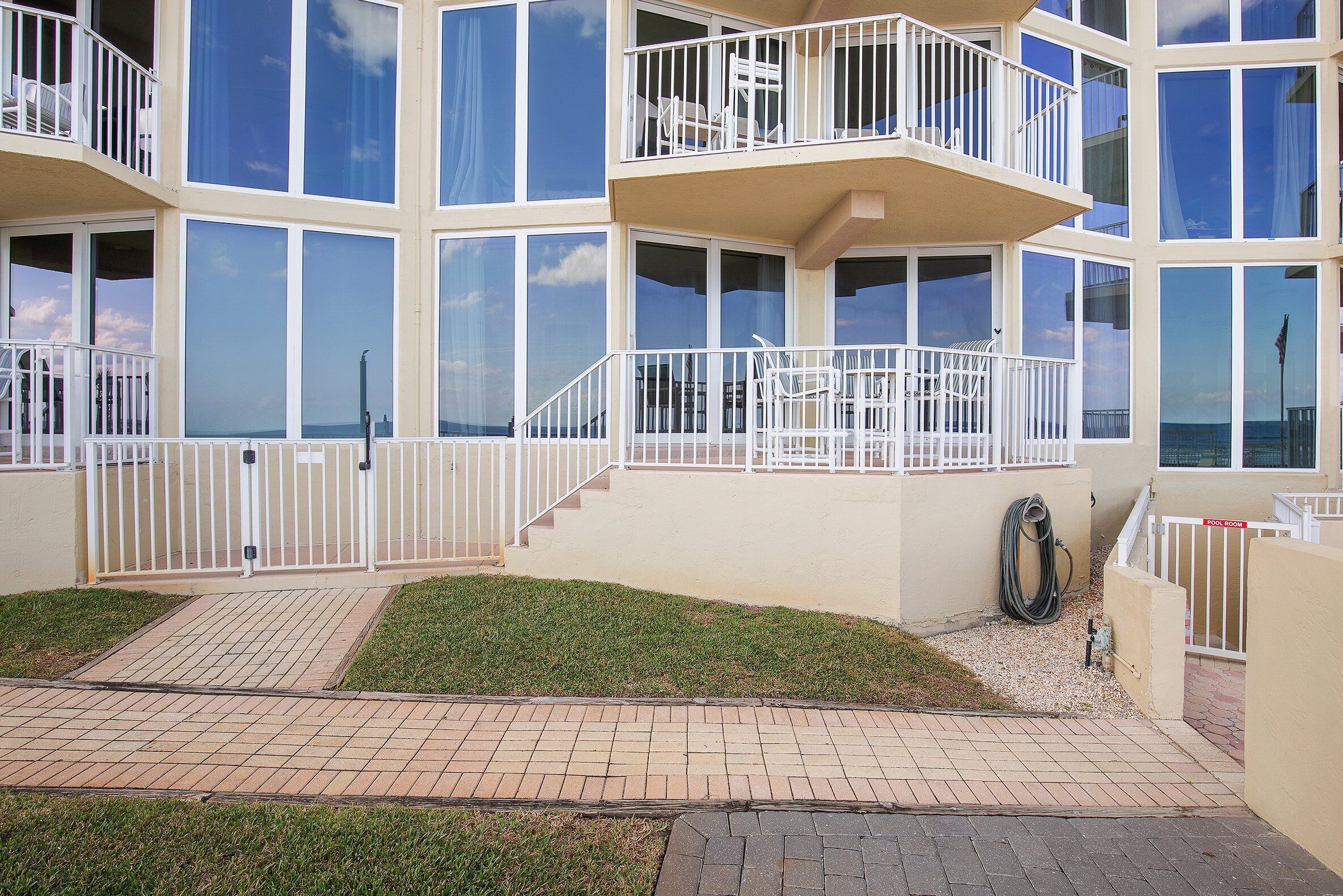 A multi-story building with balconies, large windows, and a paved entrance area.