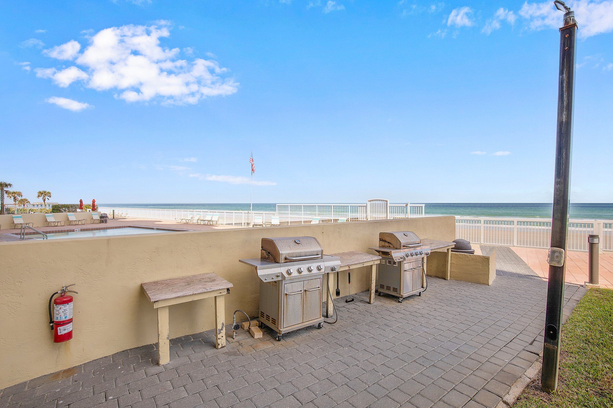 Eine Terrass mit Grill, Feuerlöscher und Poolbereich mit Liegestühlen.