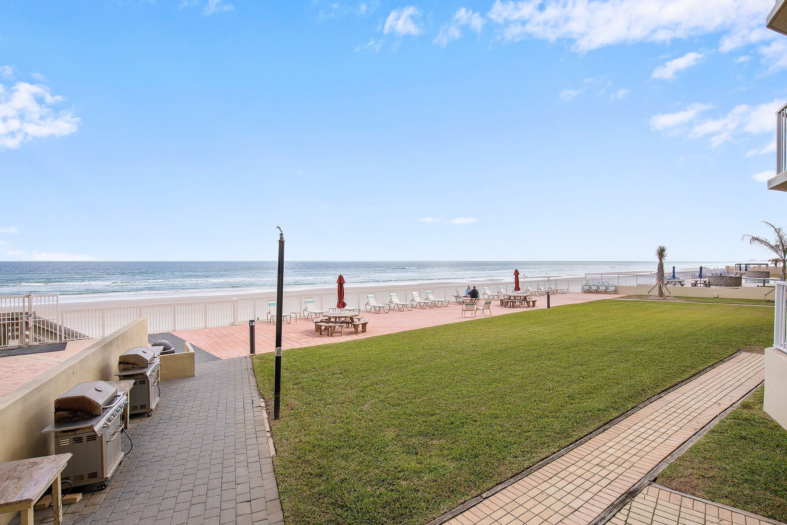 A patio area with outdoor seating, a grill, and a view of the beach.