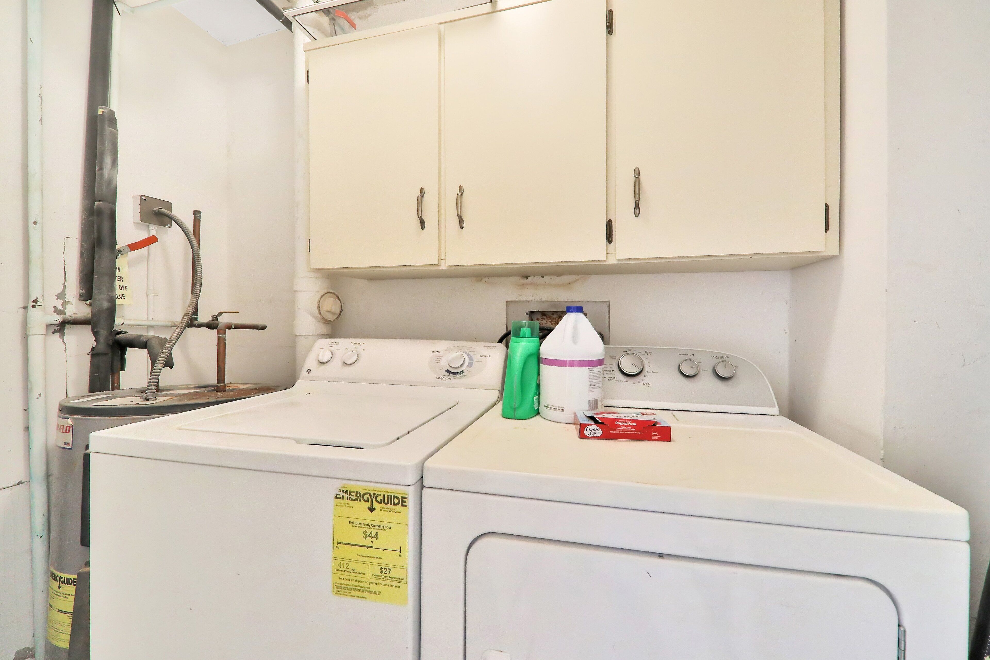 A laundry area with two washers and dryers, a water heater, and cabinets above.