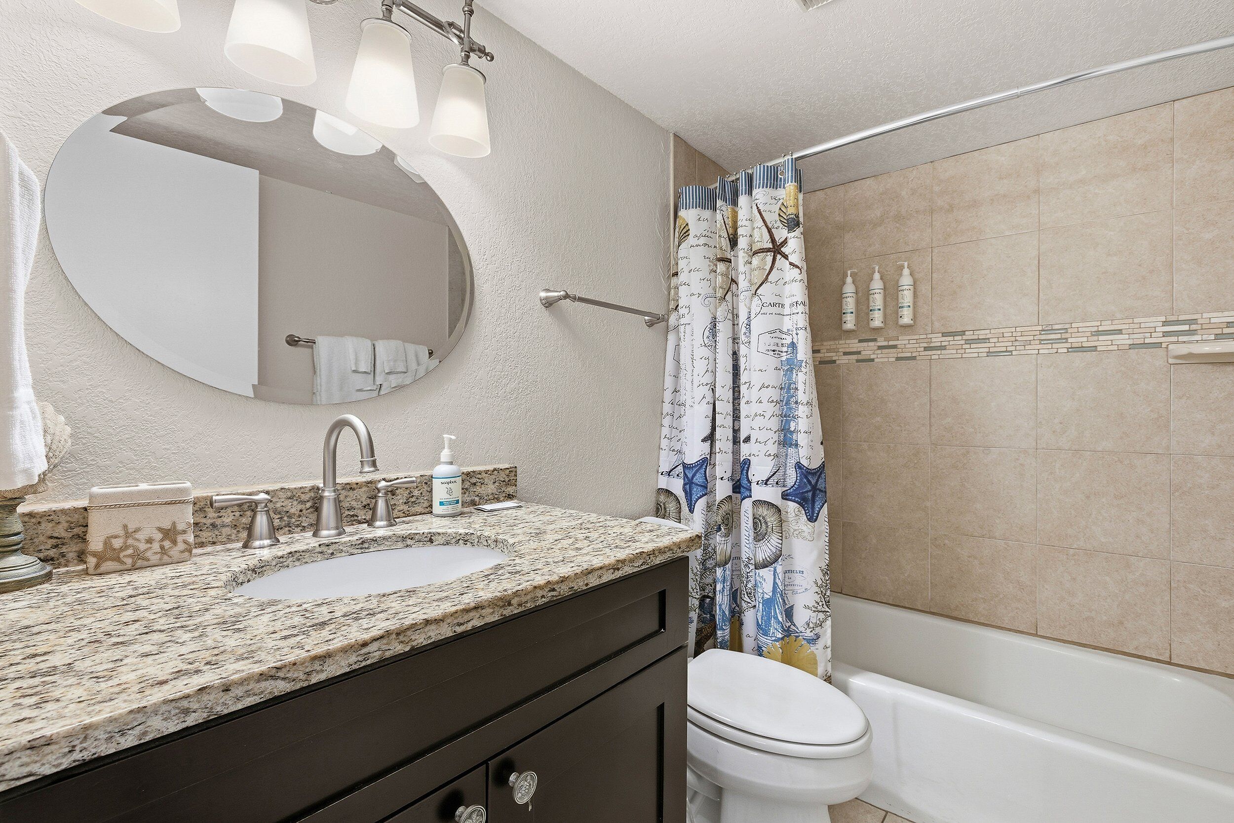 A bathroom with a granite countertop sink, a mirror, a towel rack, and a shower curtain with a nautical theme.