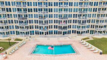 Un hôtel de grande hauteur doté de nombreux balcons, d’une piscine ornée d’un drapeau américain et de chaises longues.