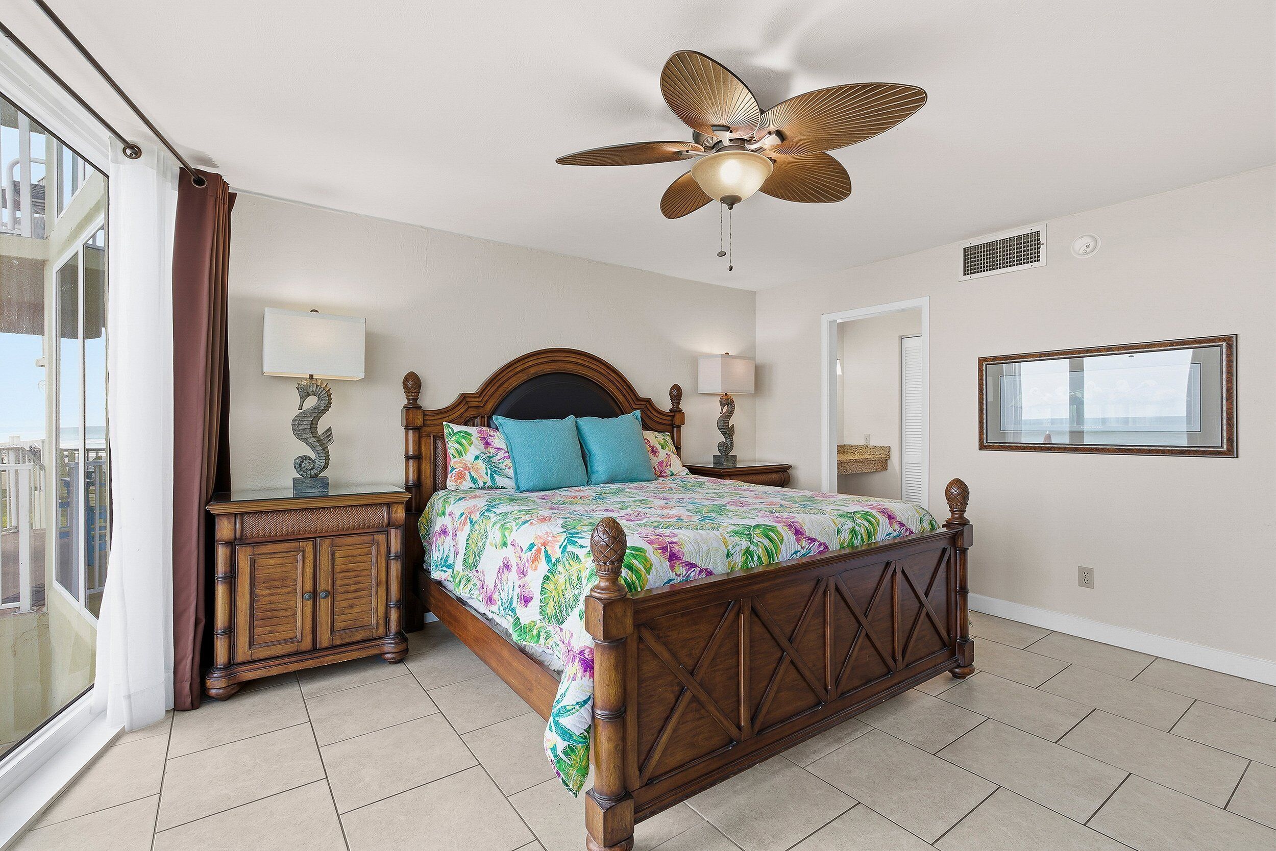 A bedroom with a wooden bed, two bedside tables, a ceiling fan, a window, and a view of the outside.