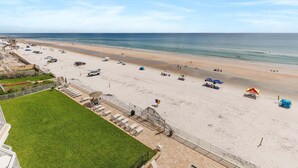 Une plage avec une zone herbeuse, une piscine et un bâtiment doté d’un balcon.