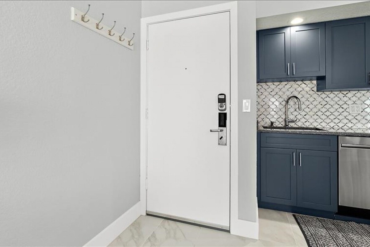Una cocina con gabinetes oscuros, un lavamanos de acero inoxidable y un salpicadero de azulejos.