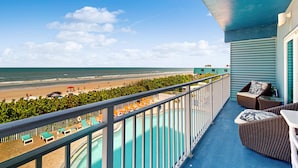 Un balcón con vistas a la playa y al océano, una piscina y mobiliario exterior.