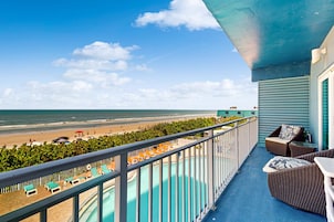 Een balkon met uitzicht op het strand en de oceaan, een zwembad en buitenmeubilair.