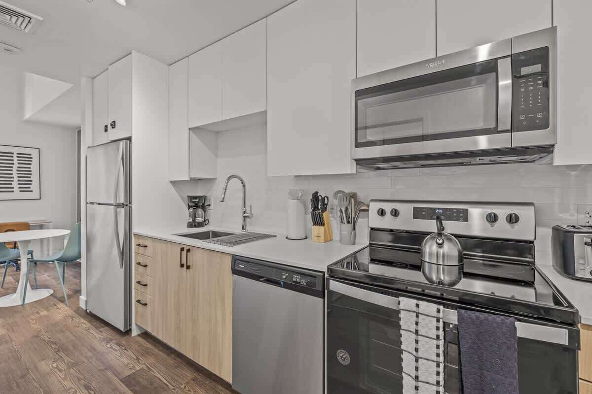 A modern kitchen with white cabinets, a stainless steel refrigerator, a microwave, a kettle, and a dishwasher.