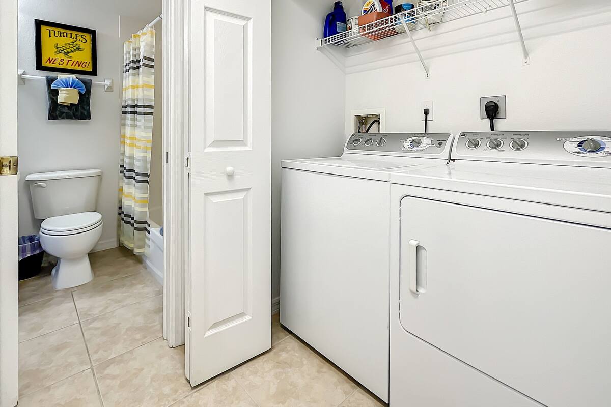 A laundry room with a washing machine, a dryer, and a shelf with cleaning supplies.