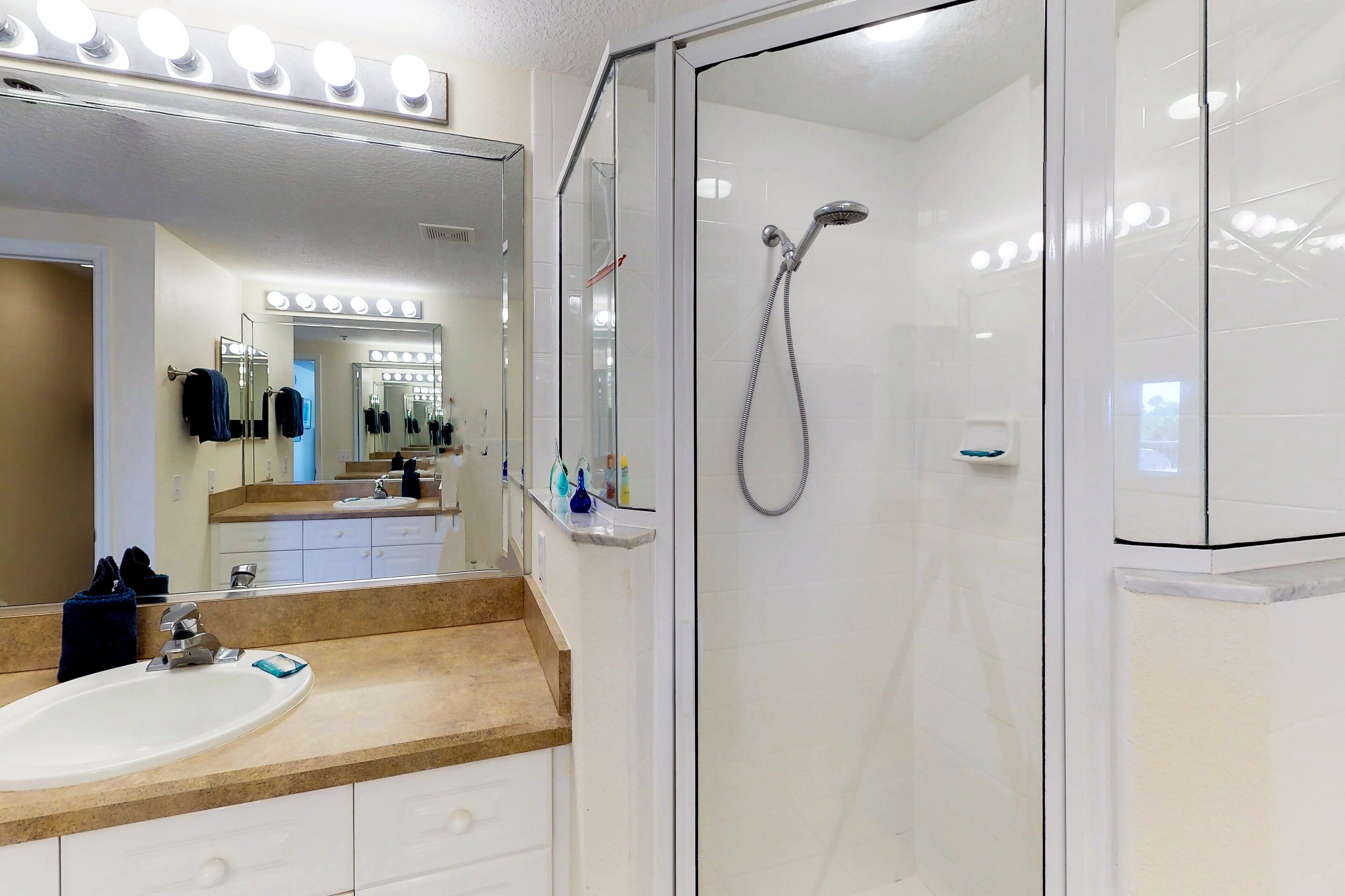 A modern bathroom with a glass-enclosed shower, a vanity with a sink, and a large mirror with lights.