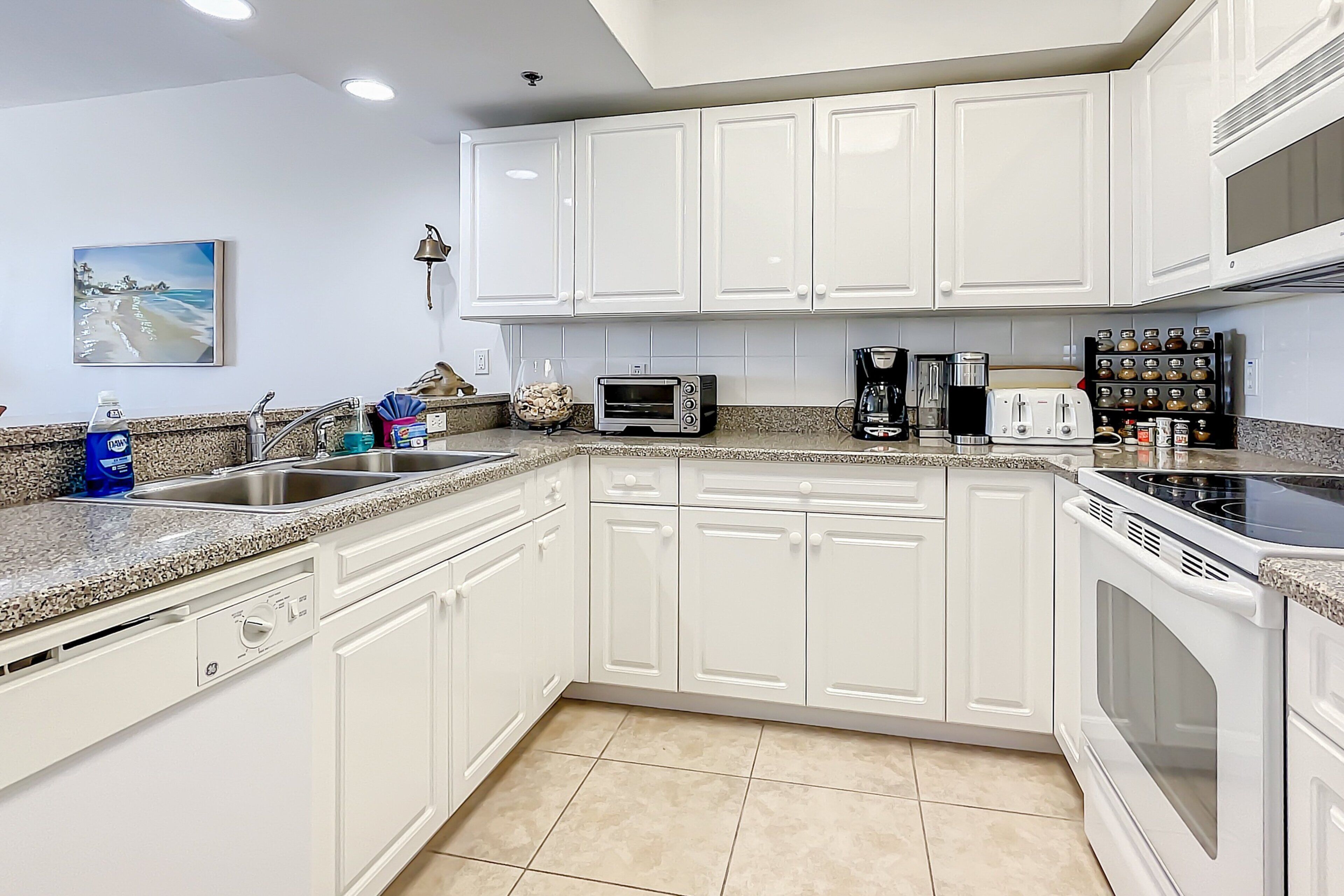 A modern kitchen with white cabinetry, a granite countertop, a built-in dishwasher, a microwave, a coffee maker, and a range hood.